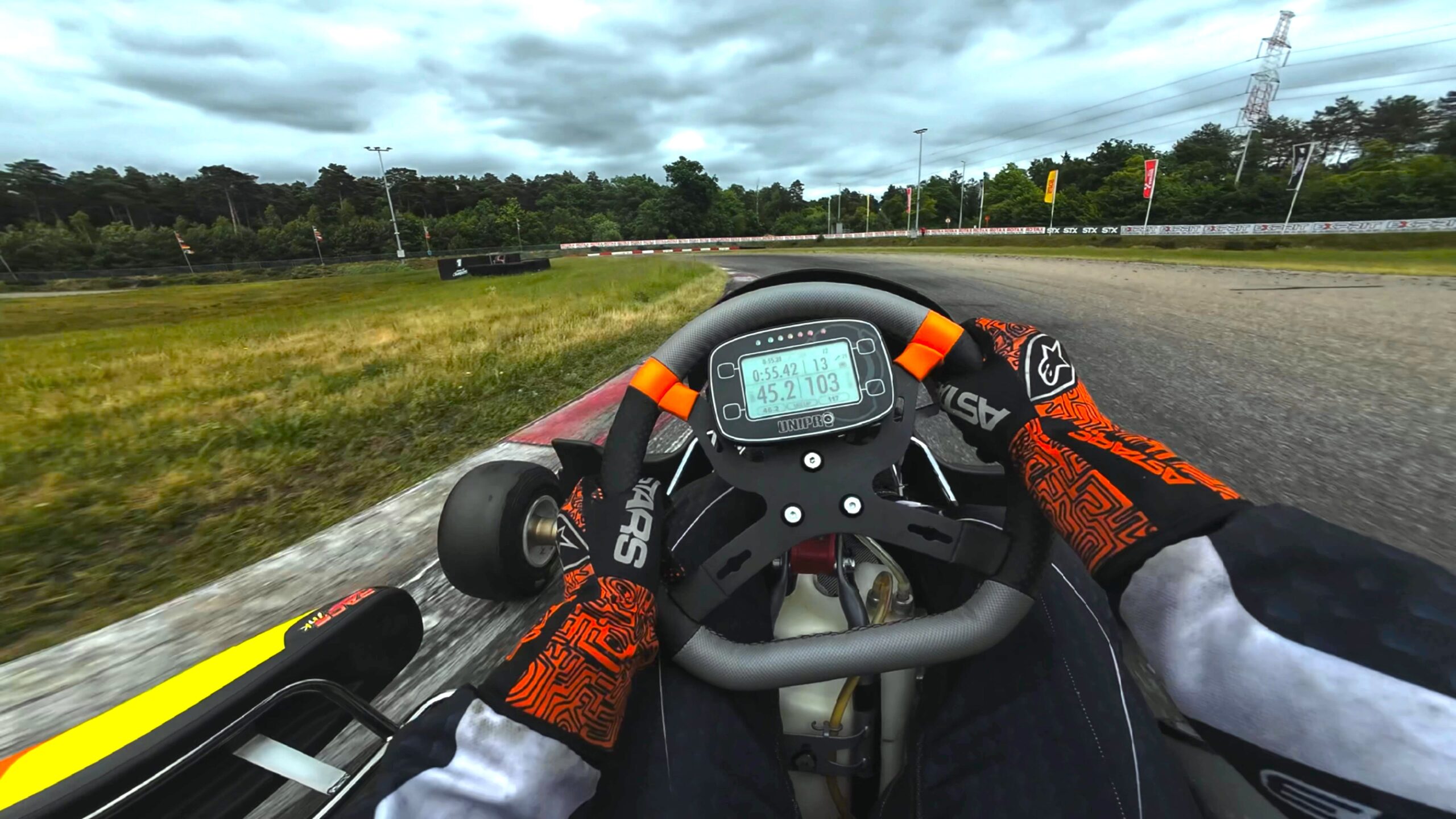 Vue à la première personne (POV) d'un pilote de karting sur circuit avec gants de protection et affichage numérique sur le volant, illustrant l'intensité du pilotage de haut niveau.