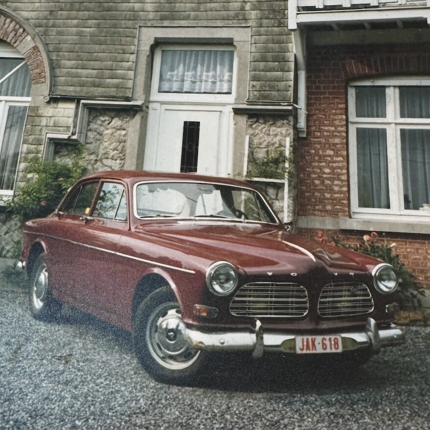 Une Volvo Amazon bordeaux classique stationnée devant une maison en pierre typique en Belgique, illustrant le début d'une collection automobile.