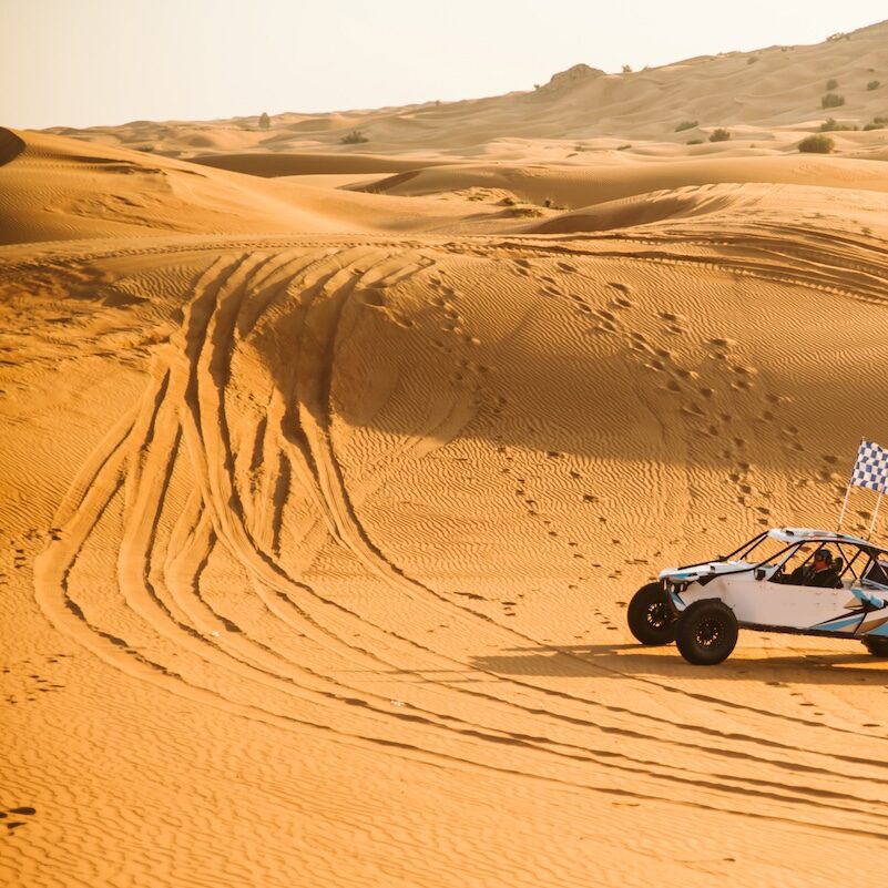 Pick-up tout-terrain au pied d'une dune de sable géante, illustrant le défi du management et de la cohésion d'équipe.