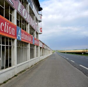 Anciens stands et tribunes du Circuit de Reims-Gueux avec publicités vintage peintes en bord de route.