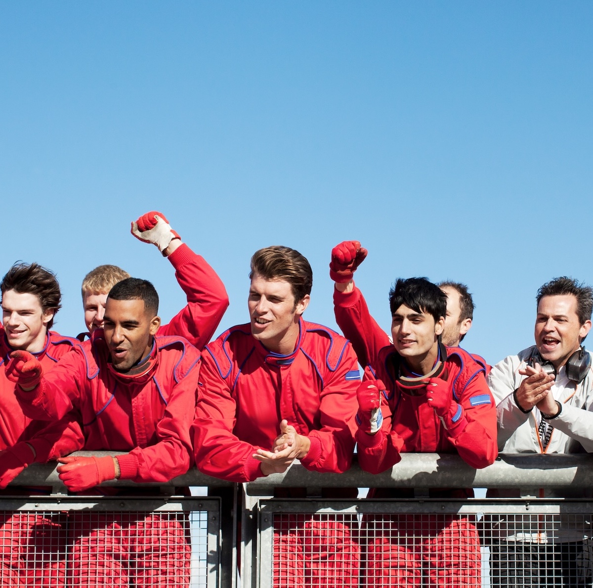 Équipe de commissaires et pilotes en combinaison rouge célébrant sur un circuit de course.