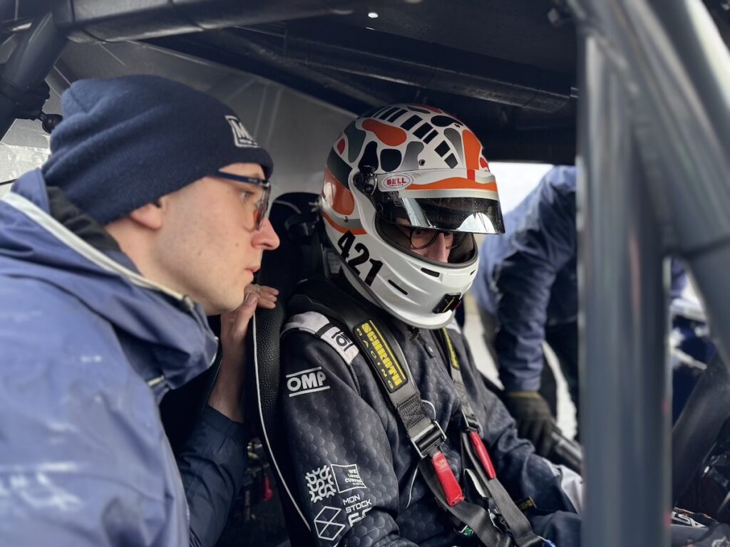 Edouard en combinaison OMP et casque Bell dans le cockpit d'une voiture de course Fun Cup avec son mécano.