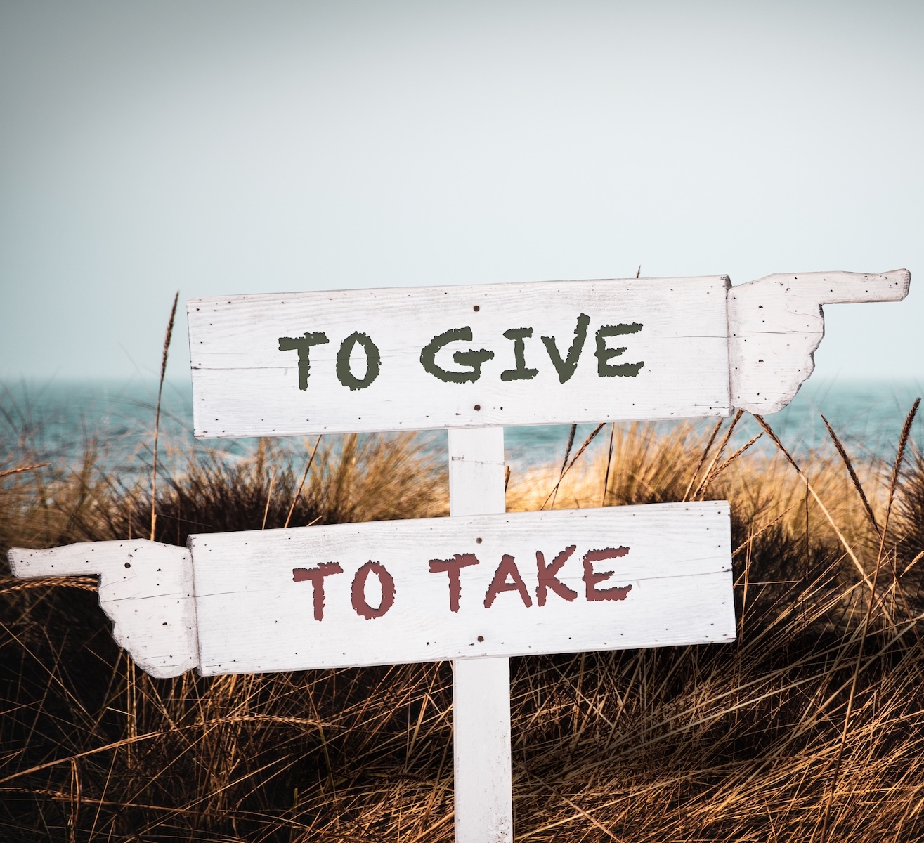 Panneau de direction en bois avec flèches pointant "TO GIVE" (donner) et "TO TAKE" (prendre) pour illustrer le choix de la solidarité.