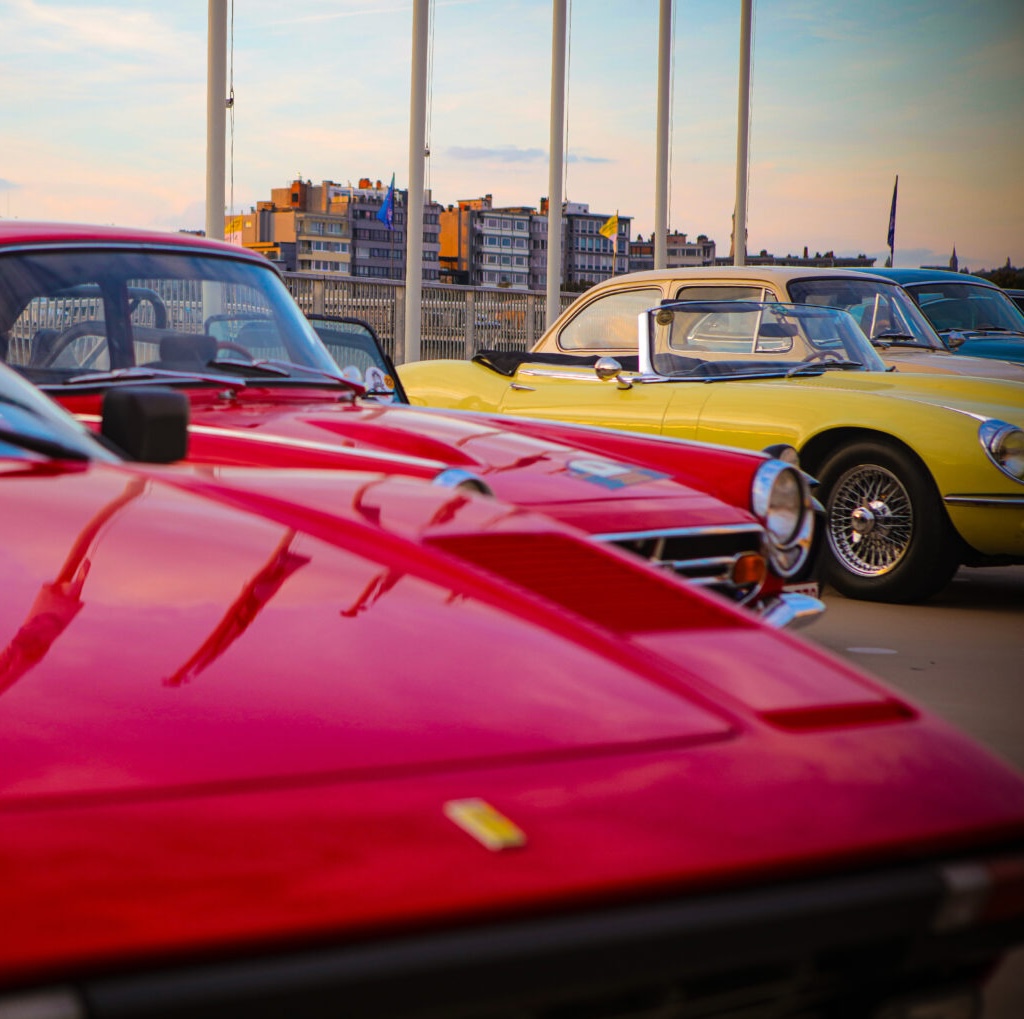 Alignement de voitures de collection classiques Ferrari et Jaguar à Liège lors d'un événement We Love Curves.